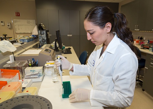 Woman in lab coat filling and preparing test tubes in laboratory.